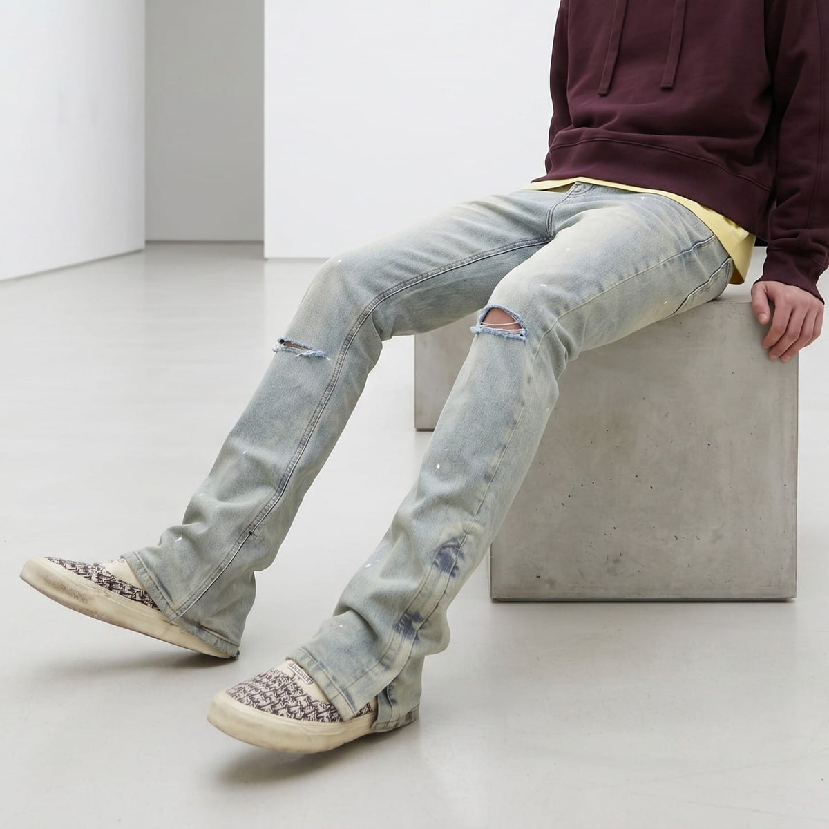 Seated model wearing light-wash distressed flare jeans with a burgundy hoodie.